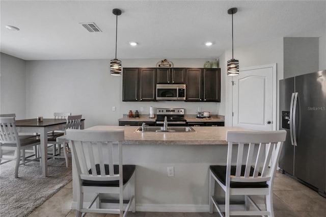 kitchen with a center island with sink, stainless steel appliances, dark brown cabinetry, and a breakfast bar area