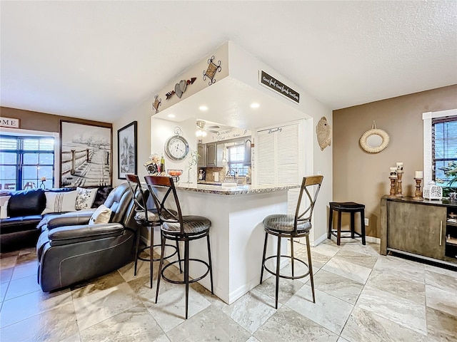 kitchen with a breakfast bar, ceiling fan, light stone countertops, a textured ceiling, and kitchen peninsula