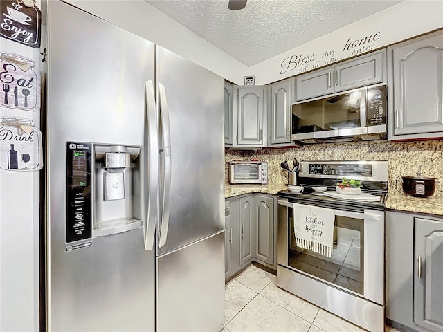 kitchen with gray cabinetry, tasteful backsplash, a textured ceiling, light tile patterned floors, and appliances with stainless steel finishes