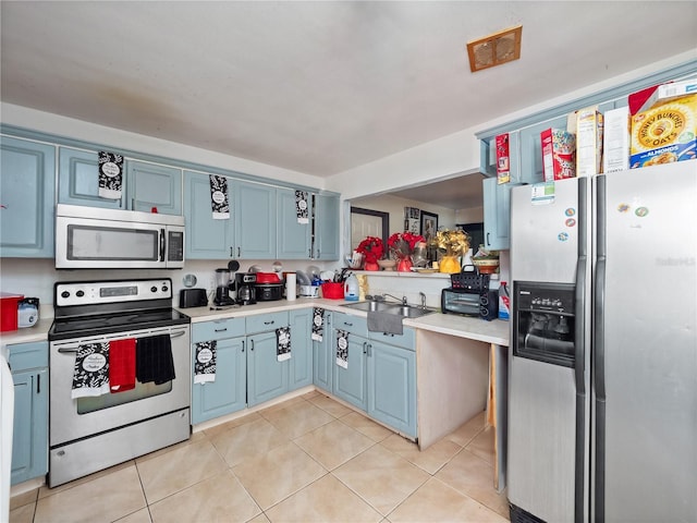 kitchen with blue cabinetry, light tile patterned floors, stainless steel appliances, and sink