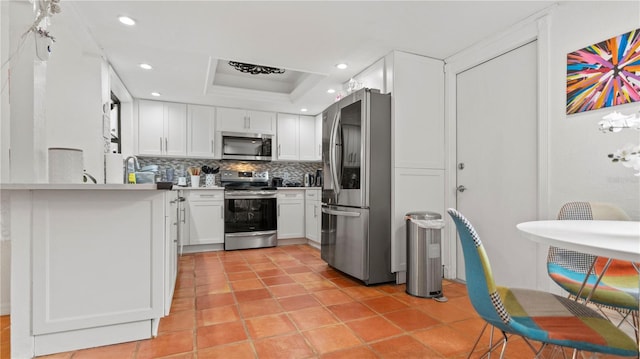 kitchen featuring white cabinets, backsplash, stainless steel appliances, a tray ceiling, and light tile patterned flooring