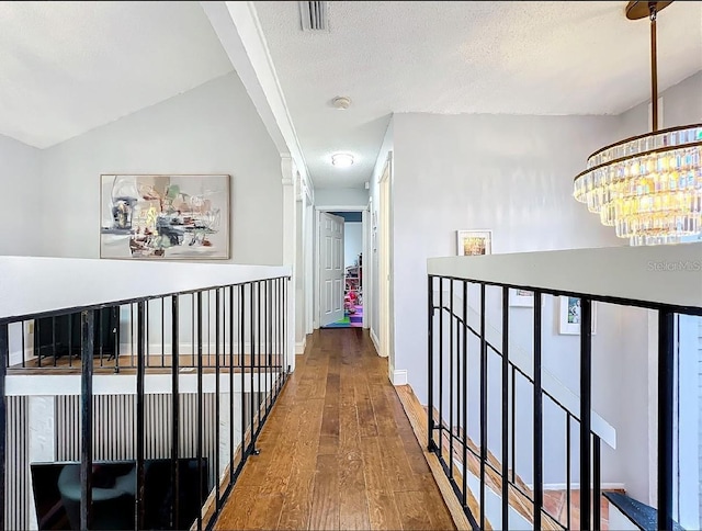 hallway featuring lofted ceiling, a chandelier, hardwood / wood-style floors, and a textured ceiling