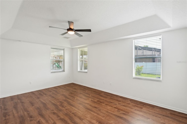 empty room with hardwood / wood-style floors, a tray ceiling, plenty of natural light, and ceiling fan