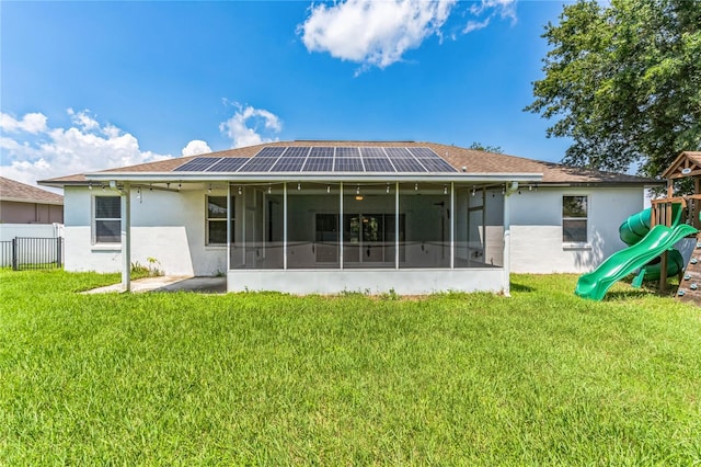 rear view of property with a playground, a lawn, a sunroom, and solar panels