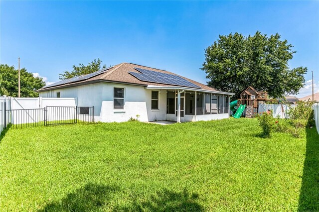 back of house featuring a lawn, a playground, a sunroom, and solar panels