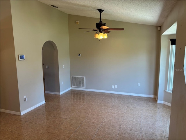 tiled spare room featuring visible vents, a ceiling fan, a textured ceiling, arched walkways, and vaulted ceiling