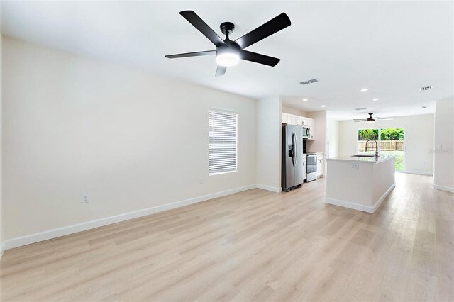 kitchen with ceiling fan, white cabinets, stainless steel fridge, an island with sink, and light wood-type flooring