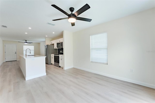 kitchen featuring appliances with stainless steel finishes, light wood-type flooring, an island with sink, white cabinets, and sink