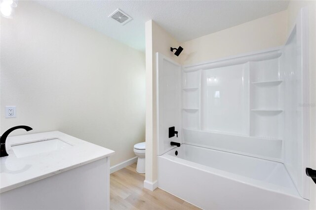 full bathroom featuring a textured ceiling, toilet, shower / washtub combination, hardwood / wood-style flooring, and vanity