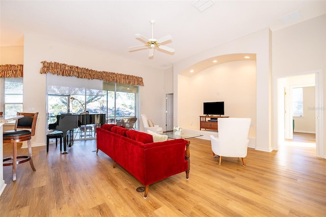 living room with light hardwood / wood-style floors, ceiling fan, and a high ceiling