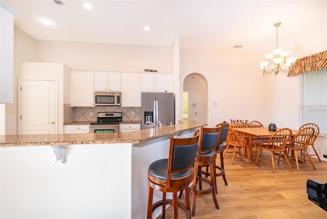 kitchen featuring a kitchen bar, an inviting chandelier, pendant lighting, stainless steel appliances, and white cabinets