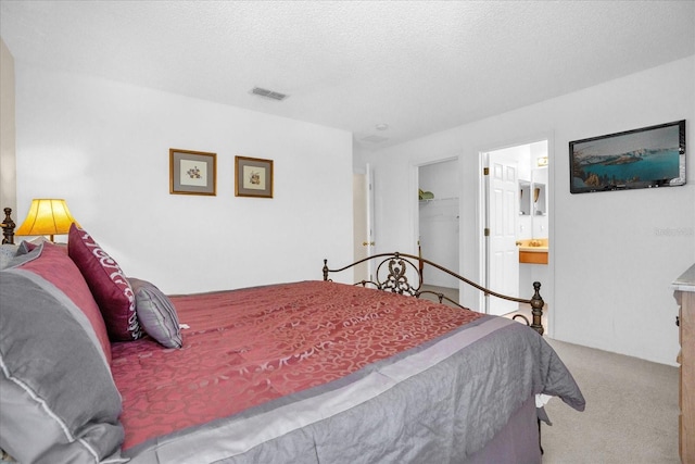 carpeted bedroom with a spacious closet, a closet, ensuite bathroom, and a textured ceiling