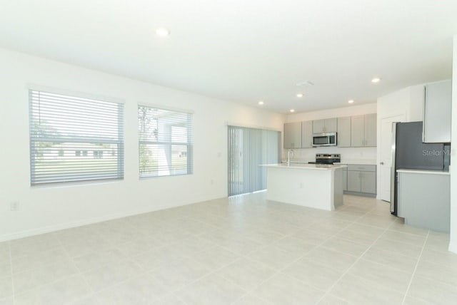 kitchen with an island with sink, light tile patterned flooring, sink, gray cabinets, and stainless steel appliances