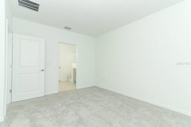 unfurnished bedroom featuring light carpet and ensuite bathroom