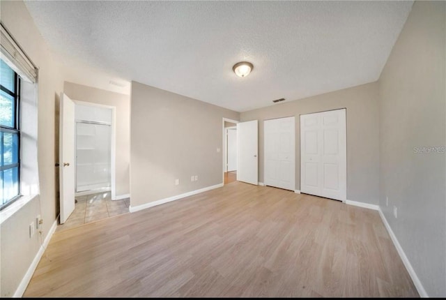 unfurnished bedroom featuring multiple closets, a textured ceiling, and light hardwood / wood-style floors