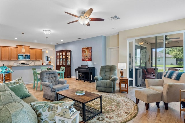 living room featuring ceiling fan, sink, and light wood-type flooring