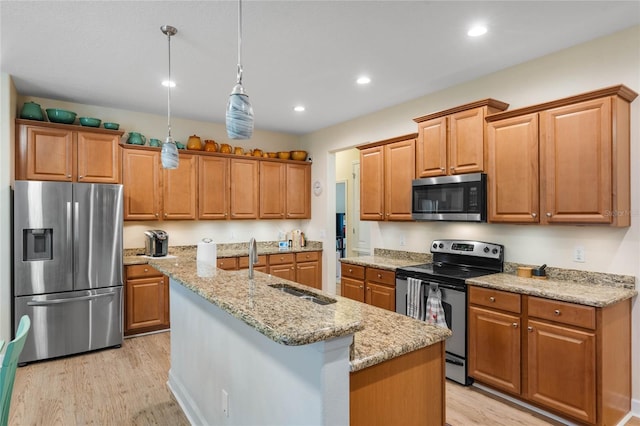 kitchen featuring a kitchen island with sink, hanging light fixtures, light stone countertops, light wood-type flooring, and stainless steel appliances