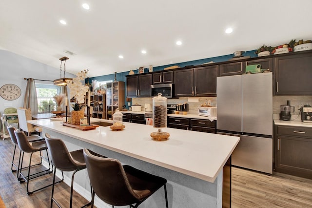 kitchen featuring a center island with sink, stainless steel appliances, hanging light fixtures, and a breakfast bar area