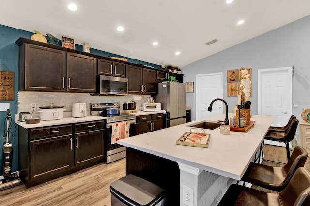 kitchen featuring dark brown cabinetry, stainless steel appliances, an island with sink, a breakfast bar, and sink