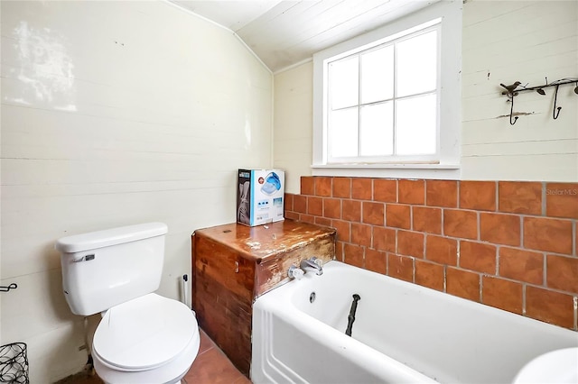 bathroom with toilet, a tub, tile walls, and lofted ceiling