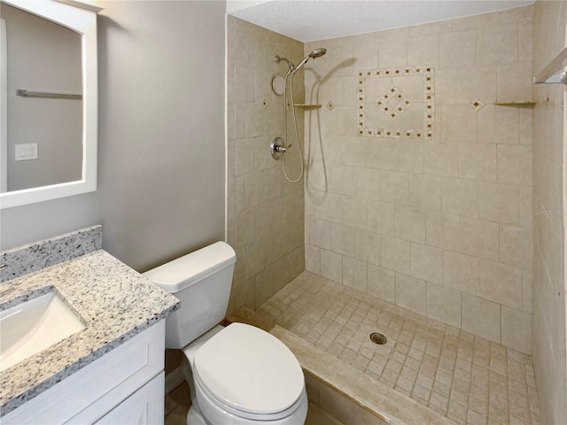 bathroom featuring a tile shower, vanity, and toilet