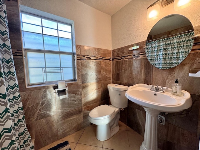 full bath featuring a textured wall, toilet, a shower with shower curtain, tile patterned floors, and tile walls