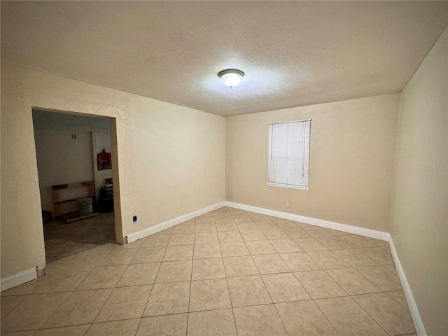 empty room with light tile patterned flooring, a textured ceiling, and baseboards