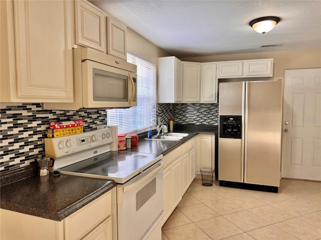 kitchen featuring white appliances, tasteful backsplash, light tile patterned floors, dark countertops, and a sink