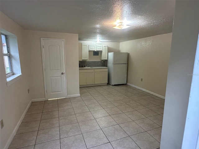 kitchen featuring freestanding refrigerator, a sink, a textured ceiling, and baseboards