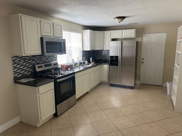 kitchen with a textured ceiling, light tile patterned flooring, appliances with stainless steel finishes, backsplash, and sink