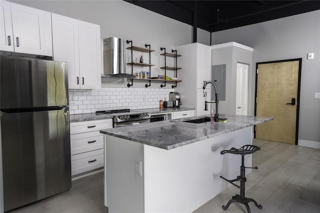 kitchen with stainless steel appliances, white cabinets, light wood-type flooring, backsplash, and wall chimney exhaust hood