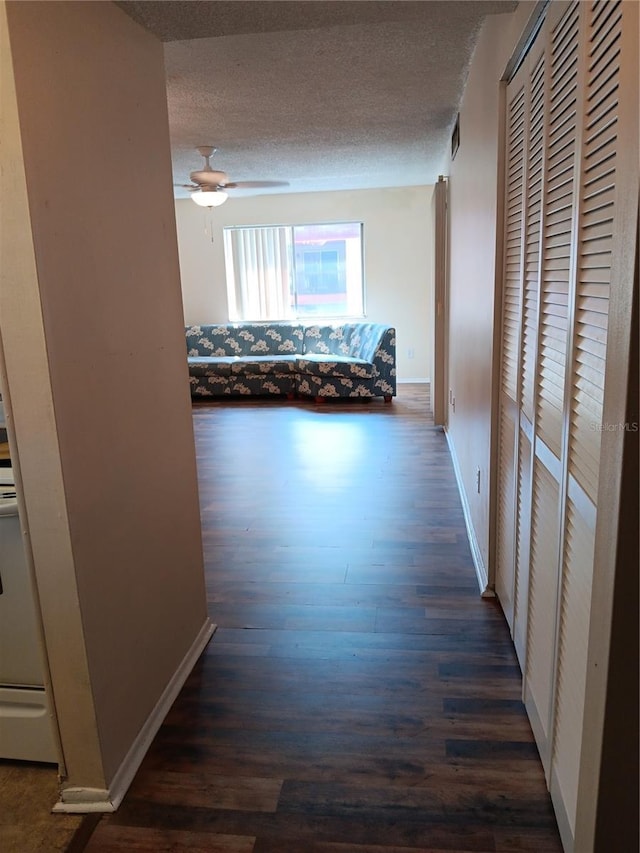corridor with dark wood-style flooring, a textured ceiling, and baseboards