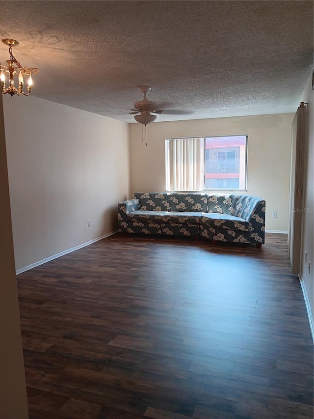 unfurnished living room featuring a textured ceiling, ceiling fan with notable chandelier, dark wood finished floors, and baseboards