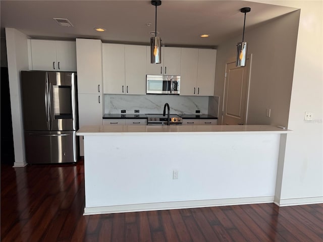 kitchen with white cabinetry, dark wood-type flooring, stainless steel appliances, backsplash, and pendant lighting