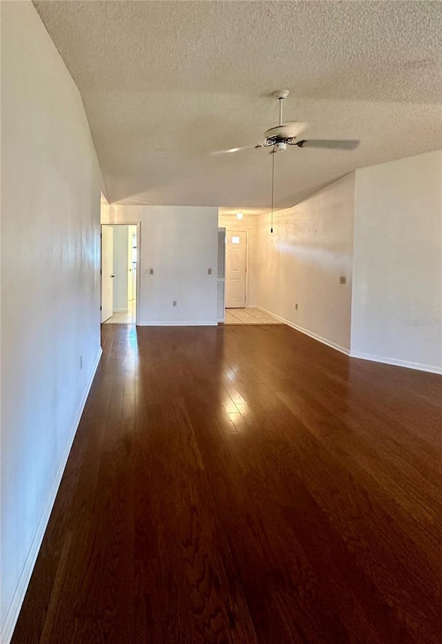 spare room featuring ceiling fan, a textured ceiling, lofted ceiling, baseboards, and dark wood-style floors