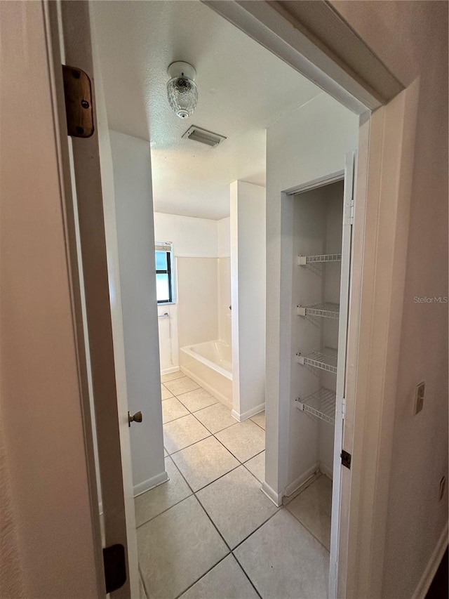 hall featuring visible vents, baseboards, and light tile patterned floors