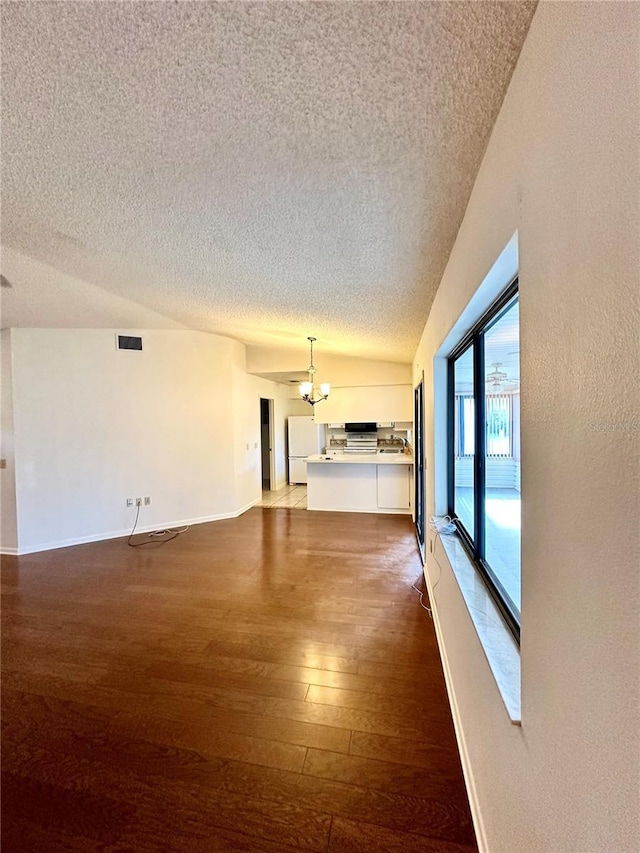 unfurnished living room featuring visible vents, dark wood-type flooring, a textured ceiling, a chandelier, and baseboards