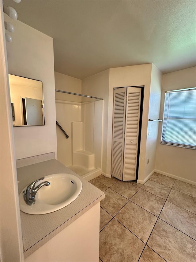 bathroom with a shower, a closet, vanity, tile patterned flooring, and baseboards