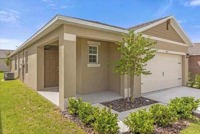 view of side of home with a garage, central AC, a lawn, and stucco siding