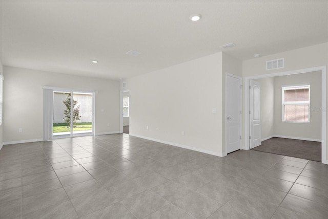 tiled spare room featuring baseboards, visible vents, and a healthy amount of sunlight