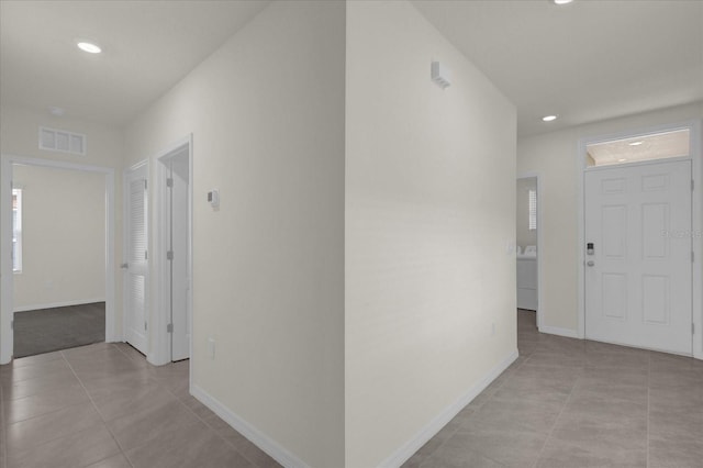 corridor with washer / dryer, baseboards, visible vents, and light tile patterned flooring