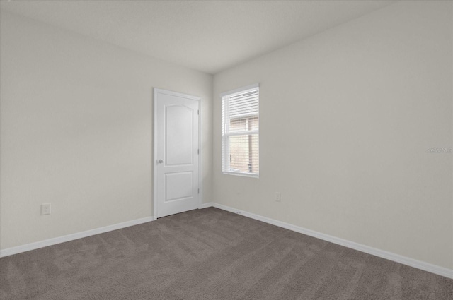 unfurnished room featuring dark colored carpet and baseboards