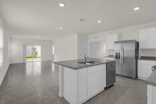 kitchen with a sink, visible vents, appliances with stainless steel finishes, an island with sink, and dark stone countertops