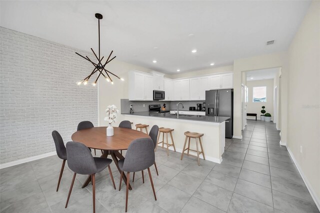 dining area with sink, light tile patterned floors, brick wall, and an inviting chandelier