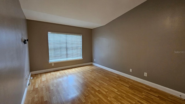 spare room featuring light wood-type flooring and vaulted ceiling