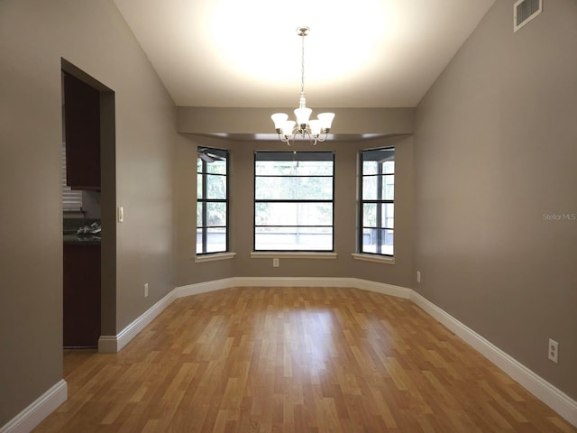 empty room featuring a notable chandelier, light wood-type flooring, and vaulted ceiling