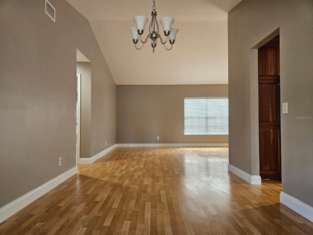 empty room featuring an inviting chandelier, lofted ceiling, and light hardwood / wood-style floors