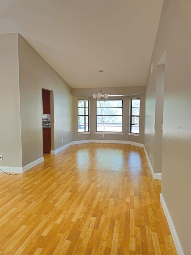 unfurnished living room with light wood-type flooring, an inviting chandelier, and high vaulted ceiling