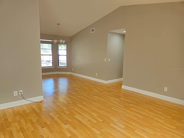 spare room with light wood-type flooring, a chandelier, and vaulted ceiling