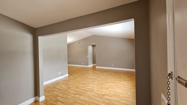 spare room featuring light wood-type flooring and vaulted ceiling